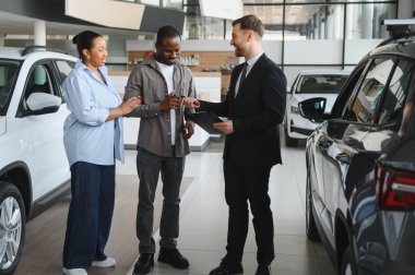 Araba galerisindeki bir satıcıdan araba anahtarı alan mutlu çift alışverişlerini tamamlıyor.