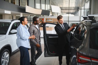 Afro-Amerikan bir çifte yeni bir arabanın özelliklerini sunan profesyonel bir araba satıcısı, onlara galeride mükemmel araçlarını seçmelerinde yardımcı oluyor.