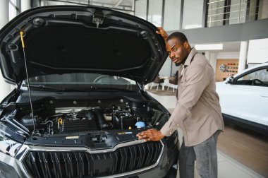 Otomobil galerisinde yeni bir aracın motorunu inceleyen adam, bilgilendirilmiş bir satın alma kararı için seçenekleri dikkatlice değerlendiriyor.