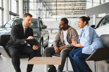 Satıcı, bir araba galerisindeki bir çifte ihtiyaçları için mükemmel yeni bir araç seçmeleri için rehberlik ediyor.