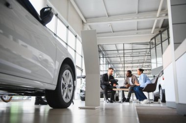 Satıcı, bir masada oturan Afro-Amerikan bir çifte araba galerisinden yeni bir araba seçiyor.