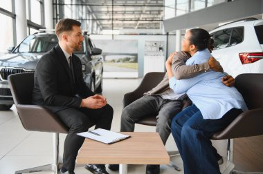 Heyecanlı çift kucaklaşıyor, galeride profesyonel bir satıcıyla araba alışverişi yapıyor.