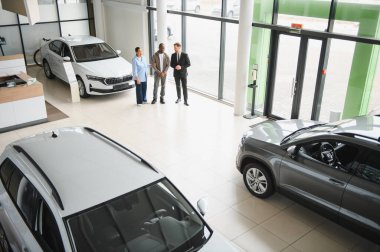 Satıcı, modern araba galerisinde araç seçen Afro-Amerikan çifte yardım ediyor.