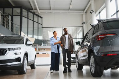 Bir araba galerisinde yürüyen Afrikalı Amerikalı çift seçenekleri değerlendiriyor ve ideal yeni otomobillerini birlikte seçiyorlar.