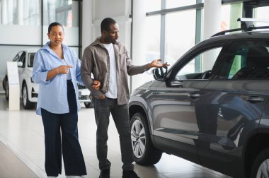 Afro-Amerikalı bir çift galeride yeni bir arabayı inceliyor, özelliklerini tartışıyor ve satın almayı düşünüyor.