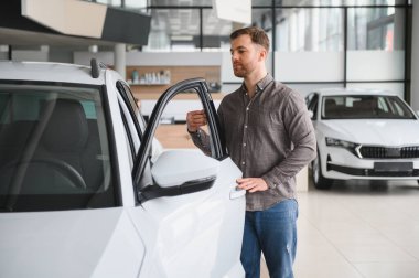 Müşteri galeride yeni bir beyaz arabayı inceliyor, kapıyı açıyor ve test sürüşüne hazırlanıyor.