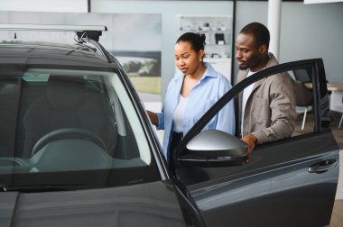 Afrika kökenli Amerikalı çiftler araba galerisinde yeni araç alımlarını ve gelecekteki sahipliklerini düşünürler.