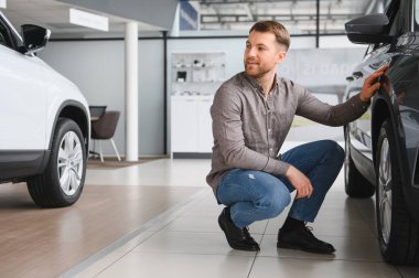 Müşteri, galeride çömelmiş ve yeni bir arabayı teftiş ediyor.