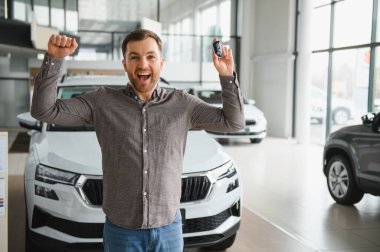 Hevesli bir adam arabanın anahtarlarını tutuyor, galeride kutlama yapıyor. Başarı ve başarıyı simgeleyen yeni araba alımı