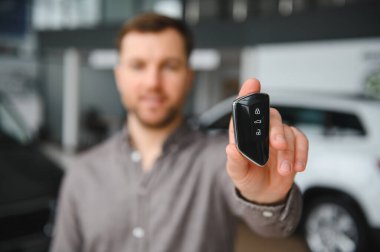 Satıcı galerinin içinde yeni bir araba anahtarı sunuyor. Yeni bir araç almanın heyecanını kutluyor.