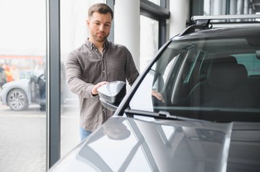 Modern bir araba galerisinde yeni bir araç satın almayı düşünürken, dikiz aynasını parlak gri bir arazi aracının içinde ayarlayan adam.