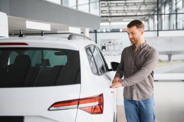 Hareketli bir araba galerisinde şık beyaz bir cipin kapısını açan adam heyecan verici bir test sürüşüne hazırlanıyor.