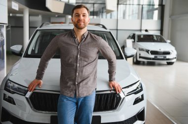 Galeride yeni bir arabaya yaslanan mutlu müşteri ihtiyaçları için doğru aracı seçiyor.