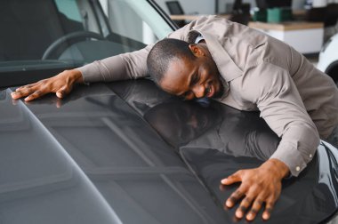 Yeni gri arabasını galeride kucaklayan heyecanlı bir adam satın almasından duyduğu memnuniyet ve neşeyi dile getiriyor.