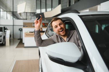 Yeni araba galerisinde arabasının anahtarlarını gösteren heyecanlı bir adam satın alımını kutluyor.