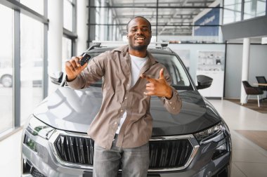 Yeni araba galerisinde araba anahtarlarını gösteren heyecanlı bir adam satın alımını kutluyor.