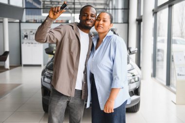 Mutlu Afro-Amerikan çifti yeni araba alımlarını kutluyorlar. Gururla araba anahtarlarını canlı bir galerinin içinde tutuyorlar.