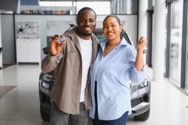 Heyecanlı çift yeni araba alımlarını kutluyor, anahtarlarını tutuyor ve galeride gülümsüyor.