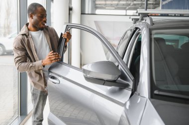 Mutlu müşteri araba galerisinde yeni bir arabanın kapısını açıyor ve satın alma kararını veriyor.