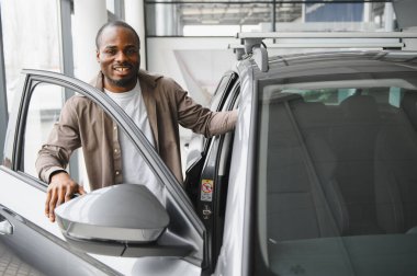 Gülümseyen adam galeride yeni bir arabanın kapısını açıyor başarılı bir satın alma ve mülkiyet yolculuğunun heyecanını kutluyor.