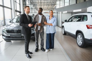 Satıcının elinde pano var. Afro-Amerikan çifte yeni araba sunuyor. Galeride.