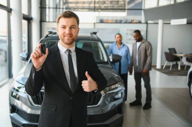 Araba satıcısı araba anahtarlarını gösteriyor ve afro-amerikan çifti de bayilikten yeni araba seçerken onaylıyor.