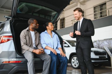 Araba satıcısı, galeriden yeni bir araba almak isteyen bir çifte araç sunuyor.