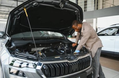 Afro-Amerikalı bir adam galeride yeni bir arabanın motorunu kontrol ediyor, satın almadan önce bilinçli bir karar veriyor.