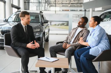 Masada oturan araba satıcısı Afro-Amerikan çifte, potansiyel müşterilere, galeri galerisine teklif sunuyor.