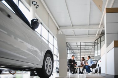 Satıcı, bir araba galerisindeki koltuklarda oturan Afro-Amerikan bir çifte yeni bir araba satın almayı tartışan bir tablet gösteriyor.