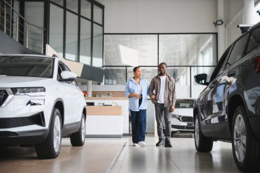 Afrika kökenli Amerikalı çift, yeni otomobillerini seçerek mutlu mesut, ferah bir araba galerisinde yürüyorlar.