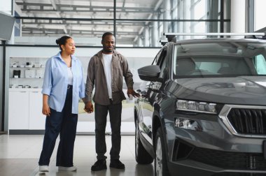 Canlı bir galeride yeni bir araba seçerken el ele tutuşan Afrikalı Amerikalı çift birlikte heyecan ve neşe yaşıyorlar.