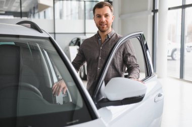 Bir galeride yeni bir arabanın kapısını açan mutlu adam başarılı bir alışveriş yaptıktan sonra gurur ve memnuniyet saçıyor.