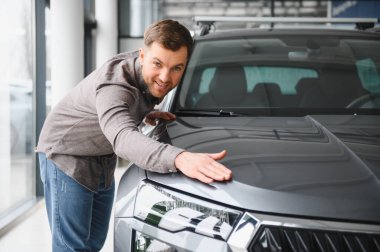 Araba galerisinde yeni gri bir cipin kaputuna dokunan mutlu müşteri yeni aracını seçiyor.