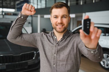 Heyecanlı müşteri yeni araba alımını kutluyor, galeride araba anahtarlarını tutuyor.