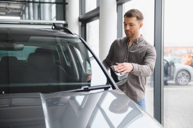 Galeride çeşitli araba özelliklerini inceleyen adam, yeni bir araç alımı seçeneklerini düşünceli bir şekilde değerlendiriyor.