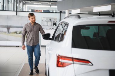 Sıradan giyinmiş bir adam, lüks, modern bir galeride yeni bir SUV 'u teftiş ediyor. Bir sonraki araç alımı için seçenekleri değerlendiriyor.