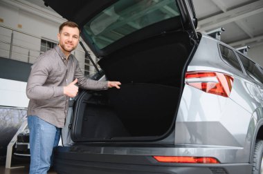 Bir galeri galerisinde yeni bir arabanın geniş bagajını incelerken mutlu adam, seçiminden duyduğu memnuniyeti dile getiriyor.