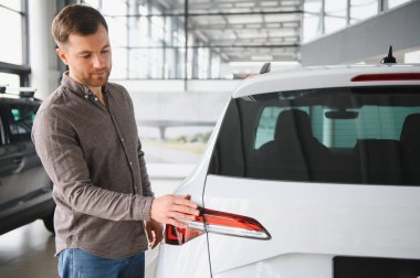 Bir araba galerisinde beyaz bir arabanın stop lambasını kontrol eden bir adam satın alma seçeneklerini göz önünde bulundurarak...