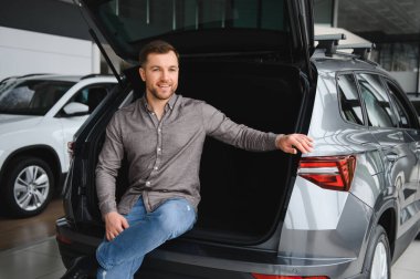 Mutlu müşteri açık araba bagajında oturuyor, boşlukları kontrol ediyor ve yeni arabasıyla aile gezileri hayal ediyor.
