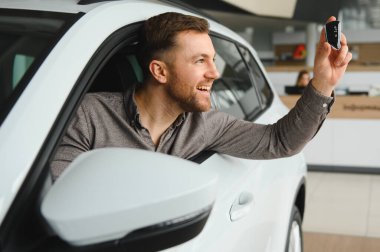 Gülümseyen müşteri galeride yeni bir arabada oturuyor, gururla arabanın anahtarını tutuyor ve sergiliyor.