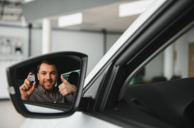 Gülümseyen adam arabanın anahtarlarını tutuyor ve yeni araç seçimiyle heyecanını ve memnuniyetini yansıtıyor.