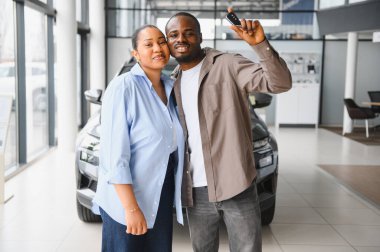 Heyecanlı çift, yeni araba alımlarını bir galeride kutluyor. Parlak yeni araba anahtarlarını neşeyle sergiliyorlar.