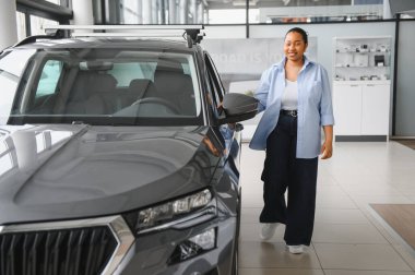 Mutlu Afro-Amerikalı kadın galeride yeni bir SUV seçiyor. İdeal aracını seçme sürecinin tadını çıkarıyor.