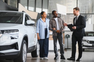 Afro-Amerikan çifte yeni bir araç gösteren profesyonel araba satıcısı, galeride alışverişi tartışıyor.