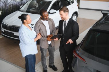 Afro-Amerikan çifte yeni araba sunan profesyonel satıcı galeride satış detaylarını tartışıyor.