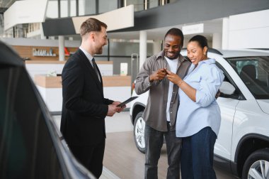 Heyecanlı çift, profesyonel bir satıcıdan yeni araba anahtarları alıyor ve bayiden satın almalarını kutluyorlar.