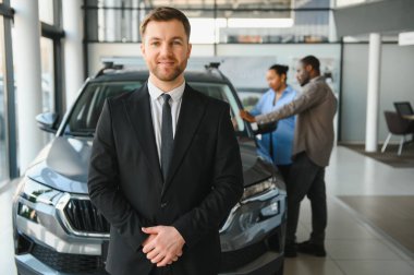 Profesyonel araba satıcısı gülümseyen Afro-Amerikan bir çifte yardım ederken modern bir galeride yeni bir araç seçiyor.