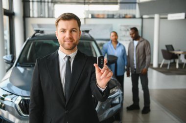 Araba satıcısı, bir araba galerisinde Afro-Amerikan bir çiftin yeni arabasının anahtarlarını tutuyor.