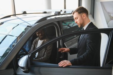 Profesyonel araba satıcısı, modern bir galeride birkaç müşteriye yeni bir arabanın özelliklerini sunuyor.